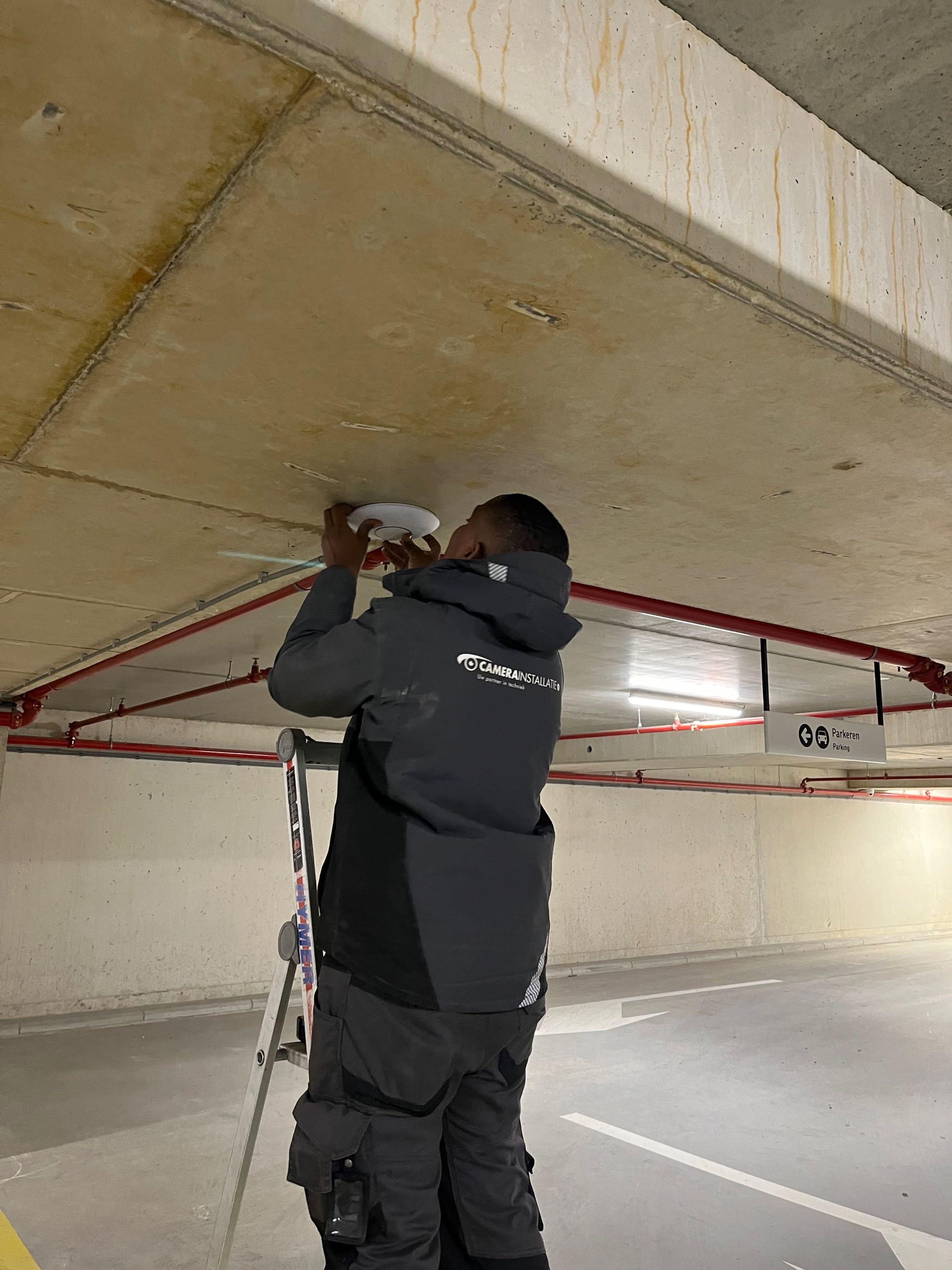 Monteur monteert een camera tegen het plafond van de parkeergarage