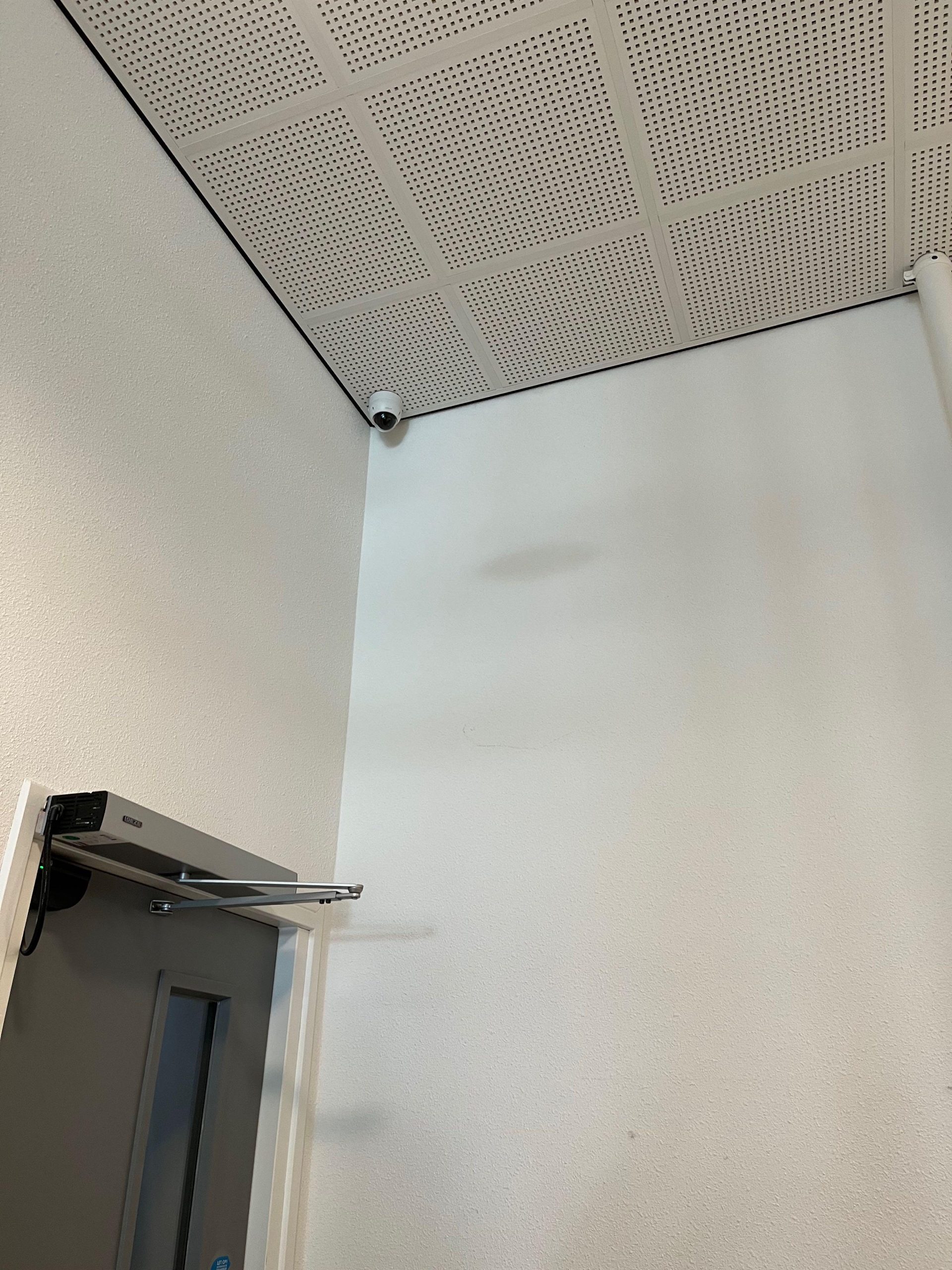 Camera in de hoek van een gang bij een deur met deurdranger in een appartementencomplex