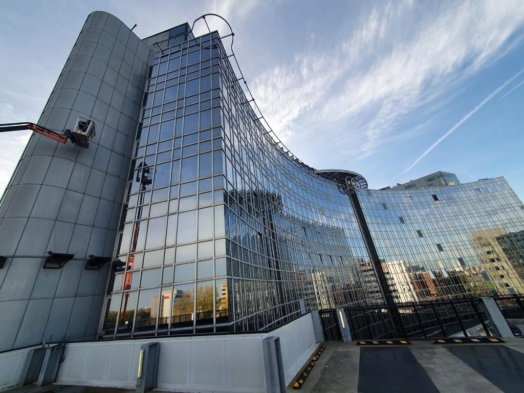 Werken met een hoogwerker langs de glasgevel van een groot complex
