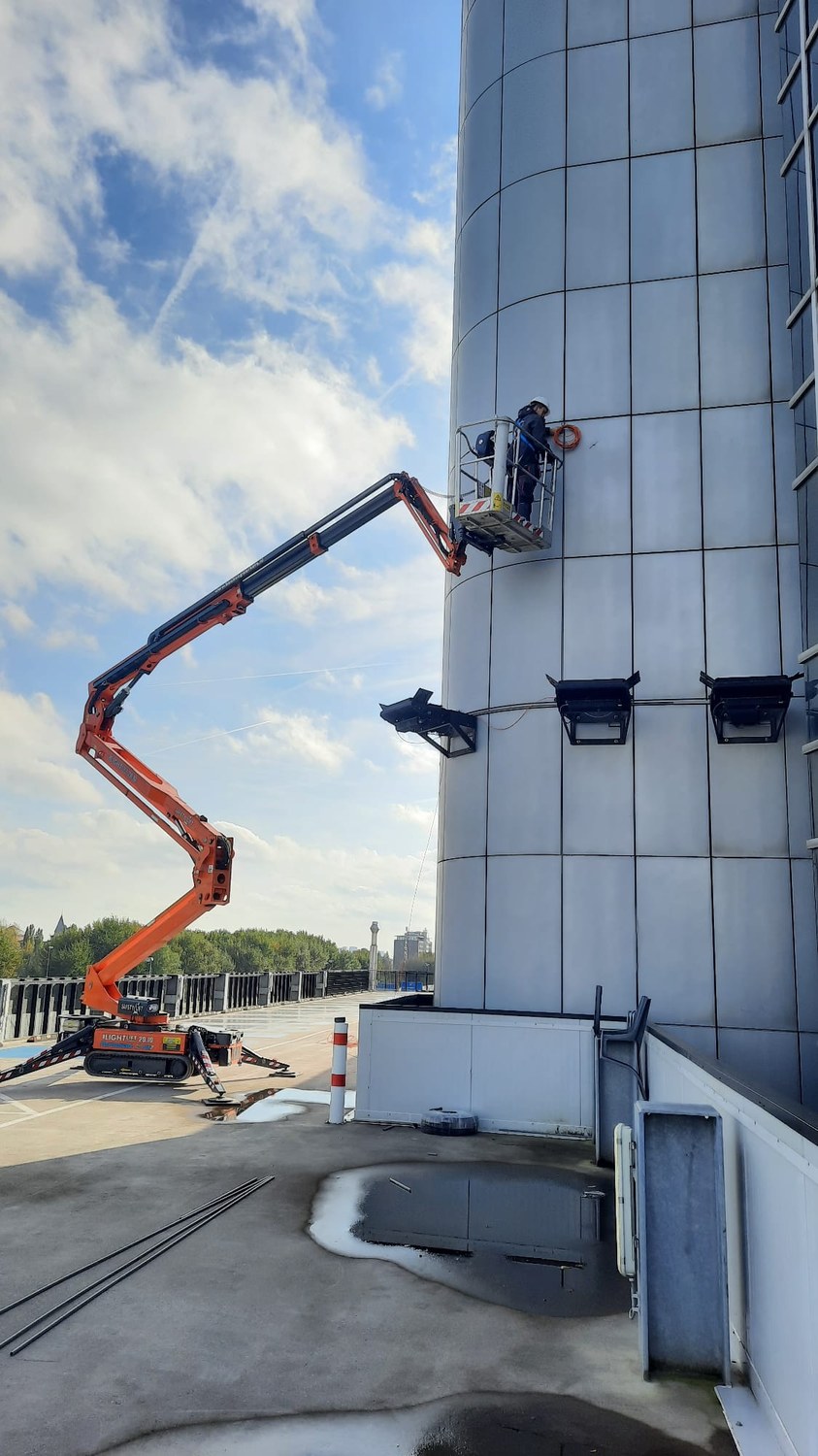 Monteur van CameraInstallatie werkt vanuit de hoogwerker aan de gevel