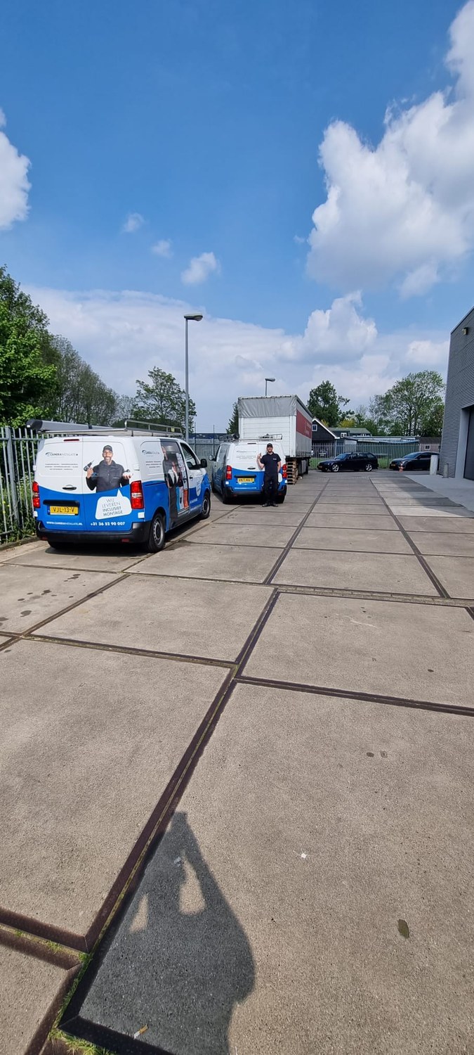 Het eigen wagenpark van CameraInstallatie op een bedrijfsterrein, met een trailer op de achtergrond