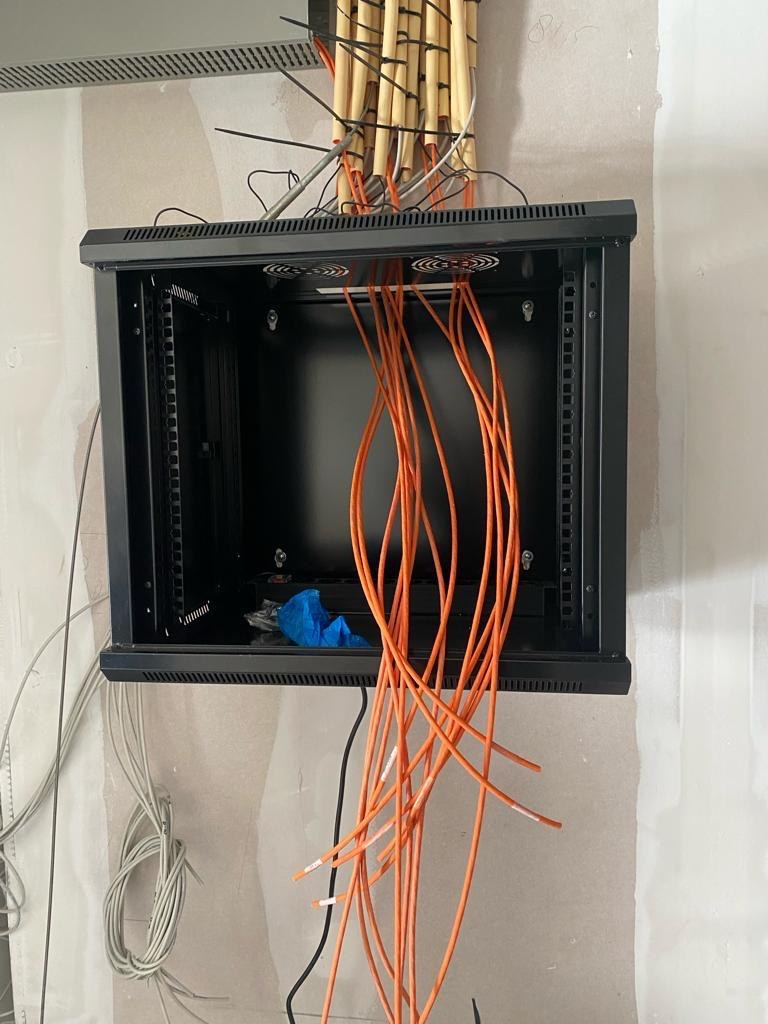 Wandkast met inkomende oranje netwerkkabels waarin bij een toegangsproject de deurcontrollers worden opgebouwd