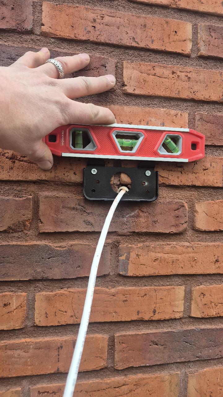 Monteur houdt een waterpas tegen de montageplaat van een camera op een bakstenen muur om hem recht af te stellen