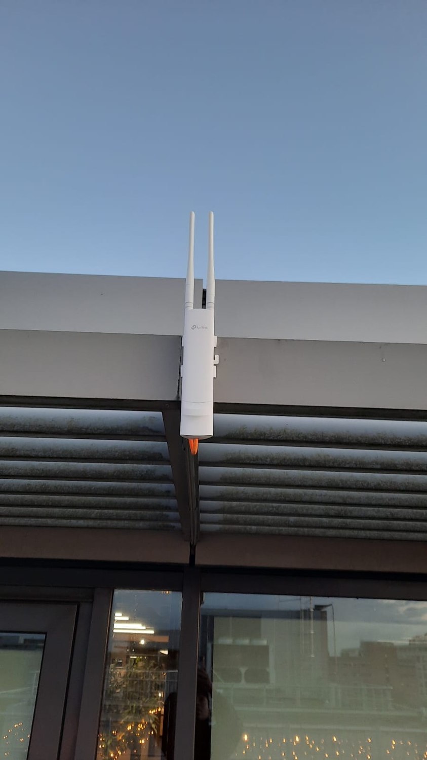 Wit TP-Link Omada buiten-access point met twee antennes, gemonteerd onder de dakrand van een gebouw