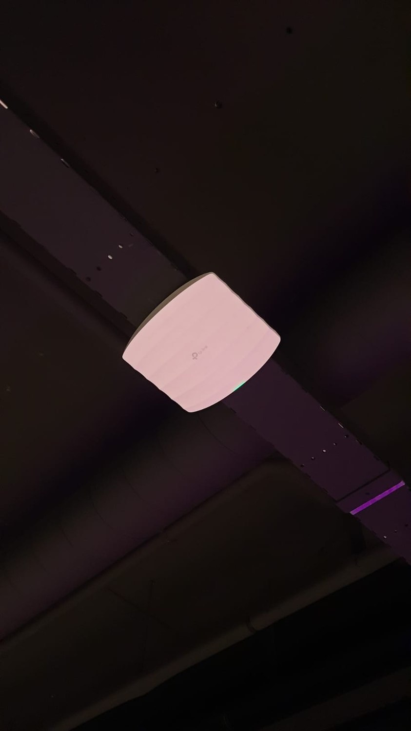 Wit TP-Link access point gemonteerd tegen een donker plafond, met een groen brandend statuslampje