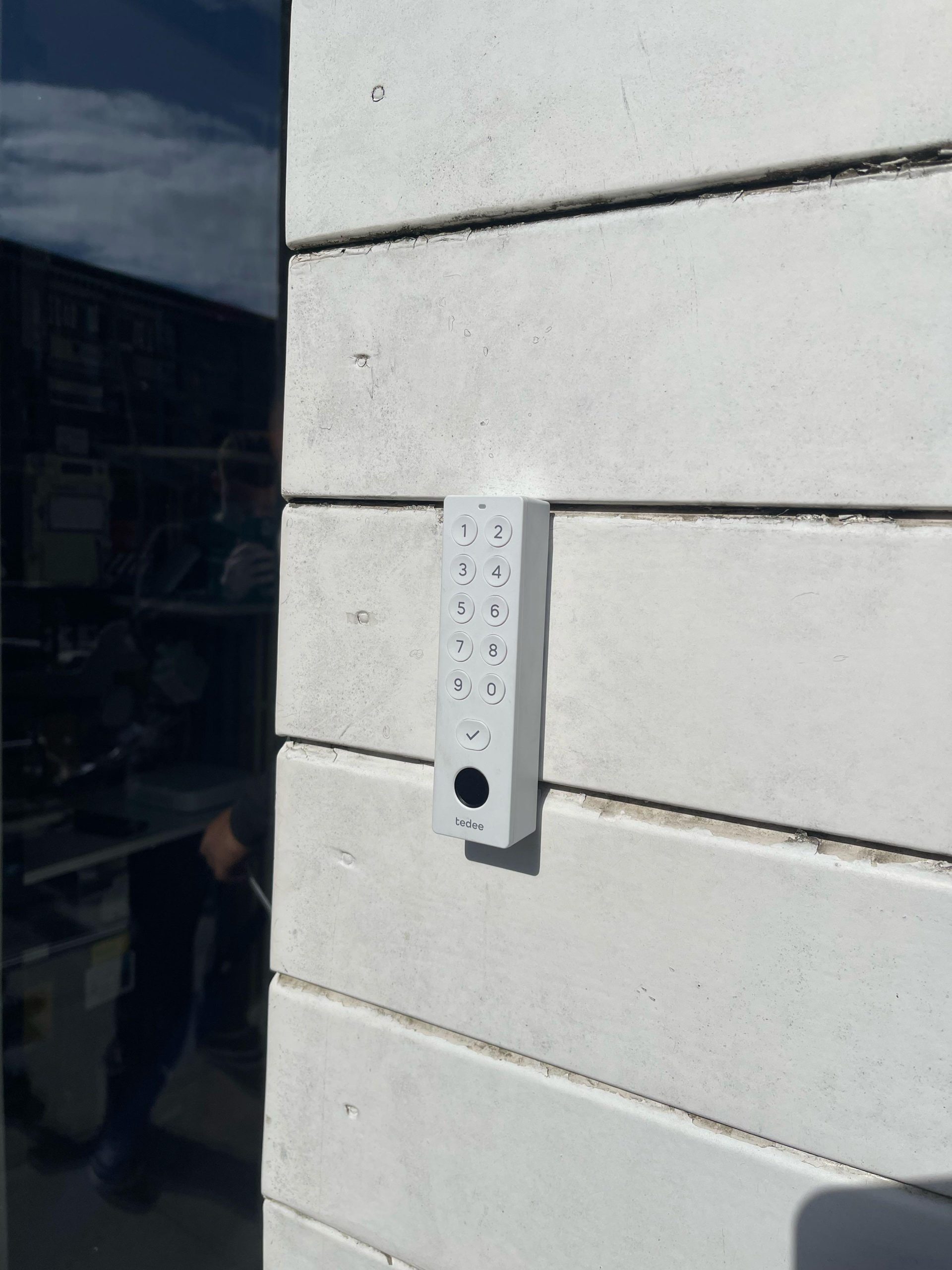 Wit Tedee keypad met cijfertoetsen en vingerafdrukscanner gemonteerd op een lichte buitengevel naast de deur