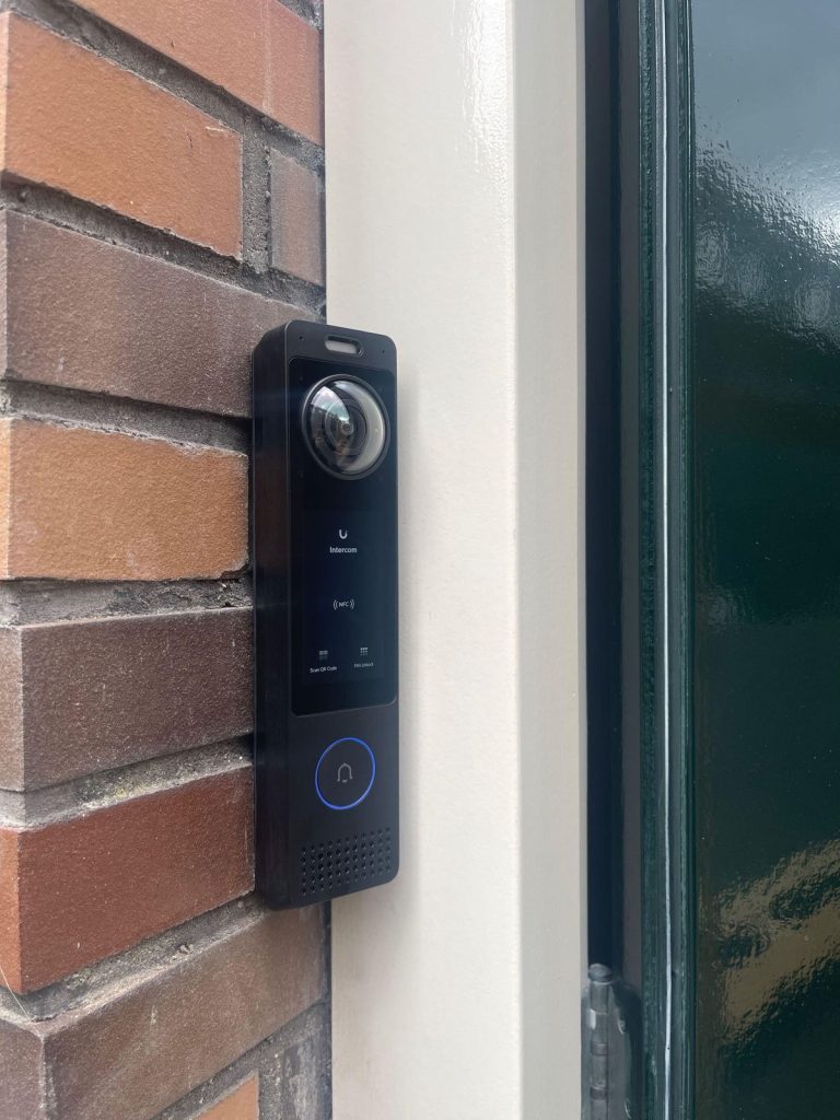 Zwarte videodeurbel met camera naast de voordeur van een woning