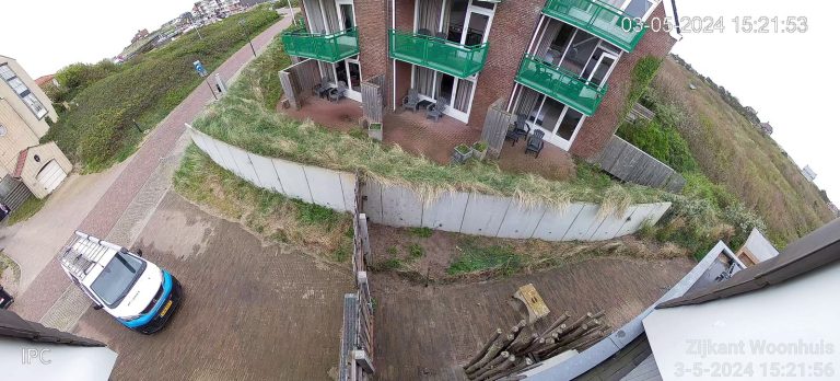 Camerabeeld van 180 graden waarop de zijkant van een woonhuis en de oprit zichtbaar zijn