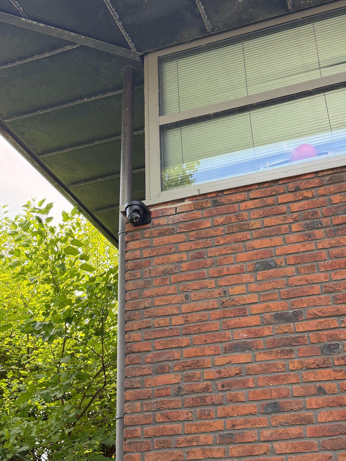 Beveiligingscamera gemonteerd onder het overstek van een woning, met de kabel langs de regenpijp weggewerkt