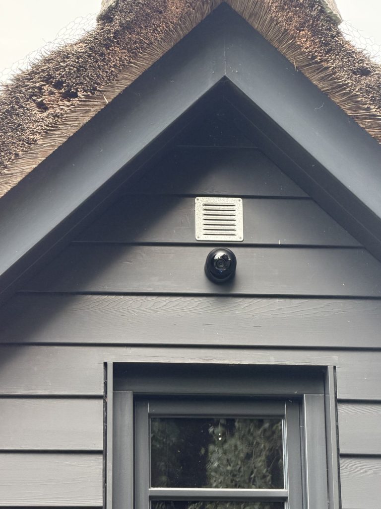 Camera op de donkere houten gevel naast het ventilatierooster, nauwelijks opvallend