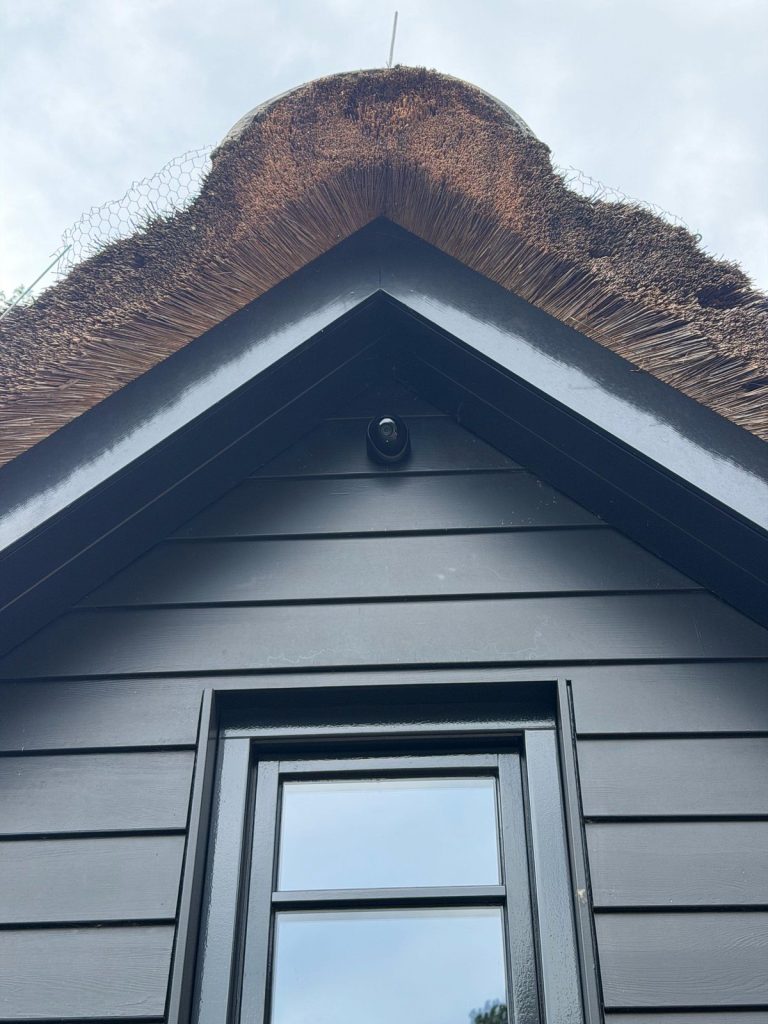 Beveiligingscamera onder de rieten kap boven een raam van een woning