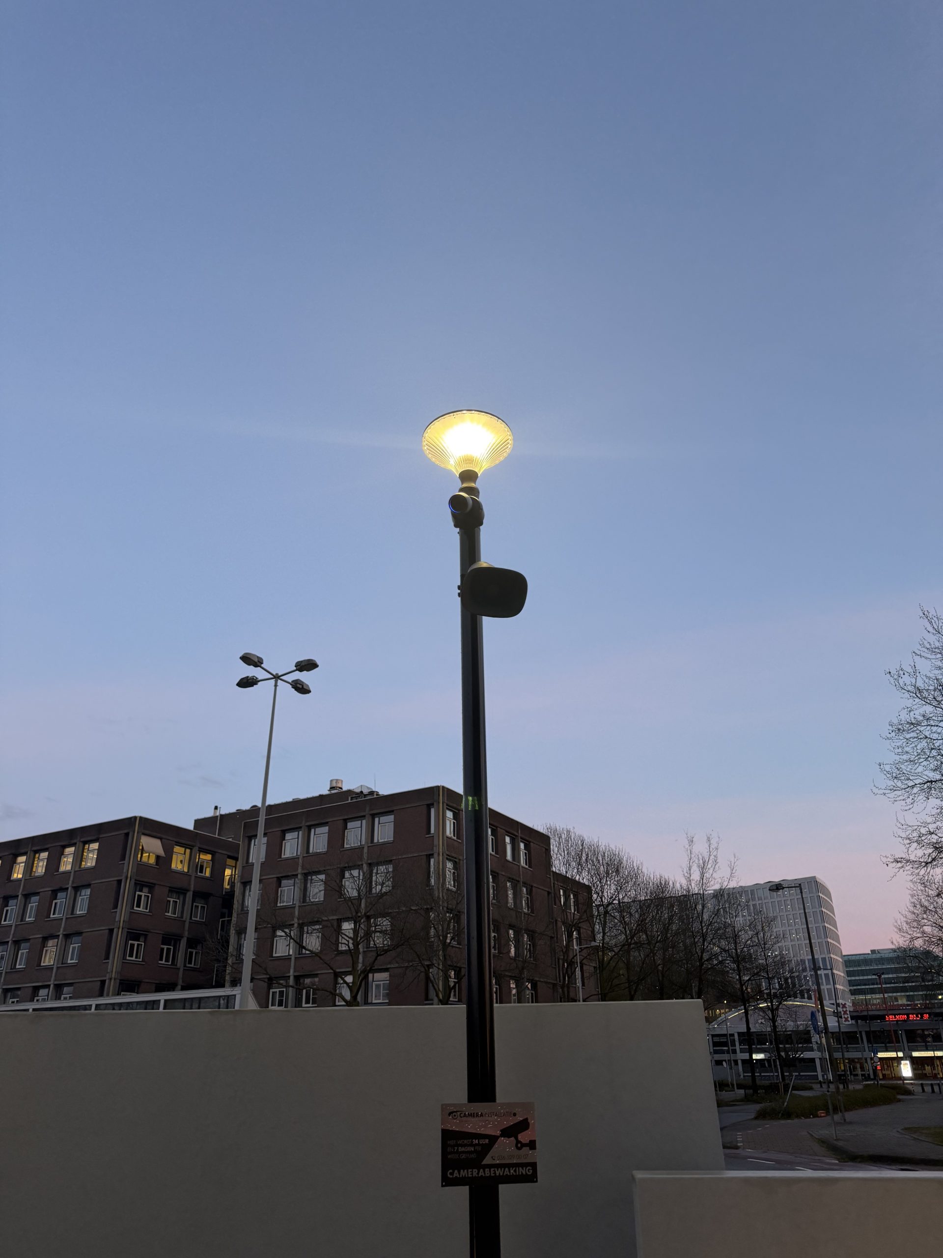 Bewakingscamera met luidspreker en een camerabewaking-bordje op een mast in de schemer