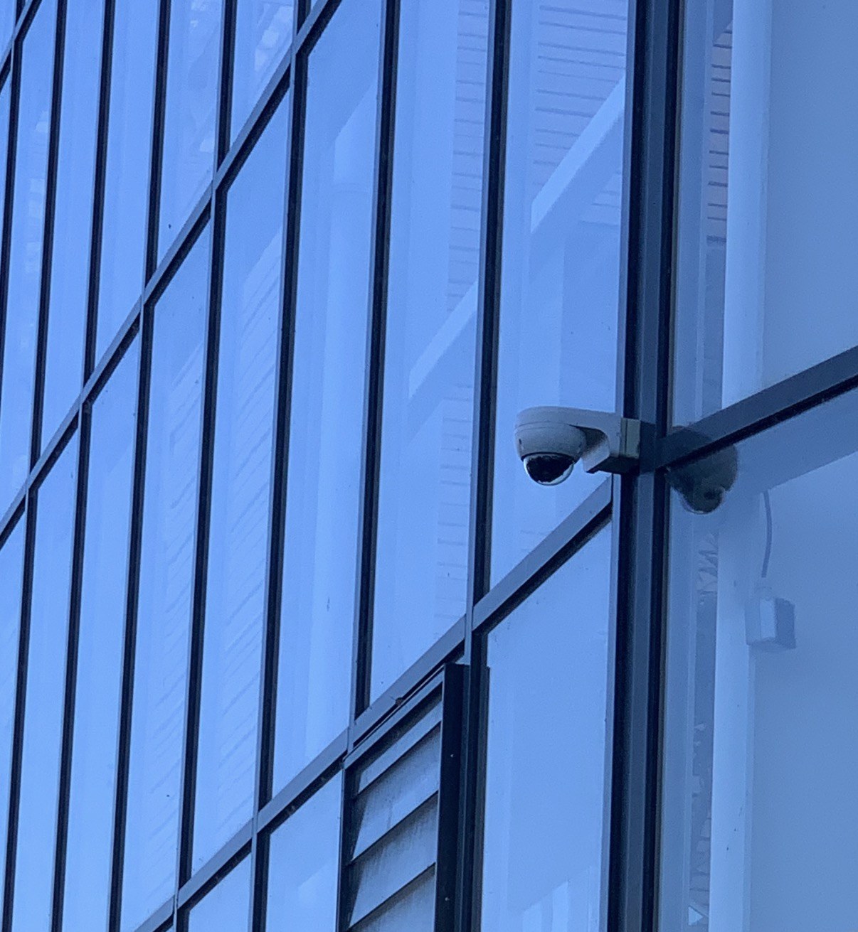 Tegen de glazen gevel van het onderwijsgebouw valt de camera nauwelijks op