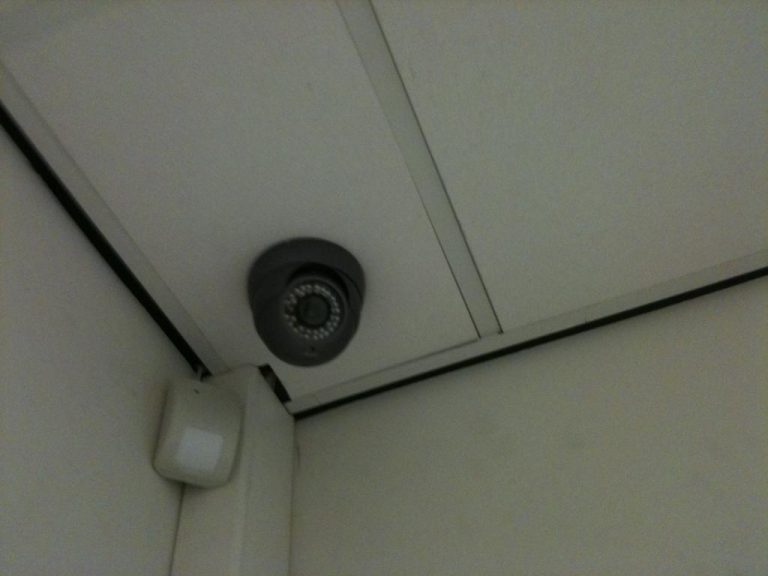 Dome-camera met nachtzicht in een plafondhoek, naast een alarmsensor
