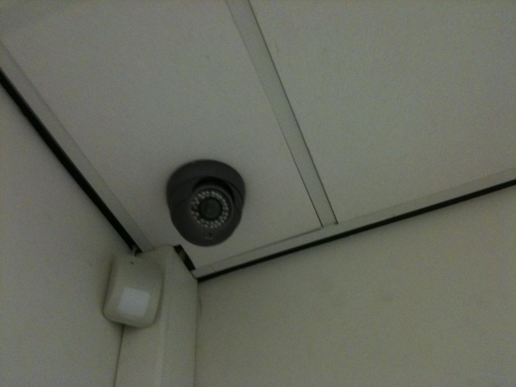 Witte domecamera met infrarood-nachtzicht in een plafondhoek, naast een bewegingsmelder
