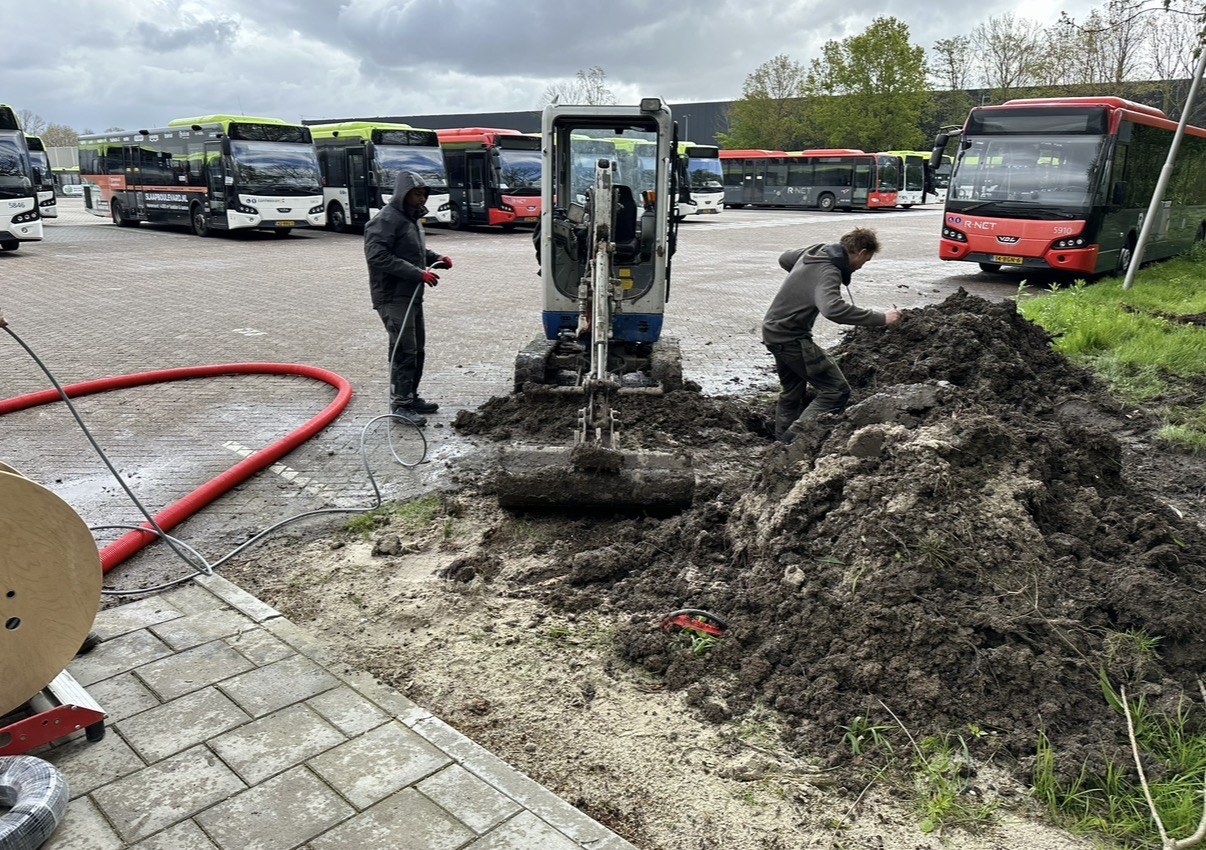 Grondwerk voor het kabeltrace op het stallingsterrein, met de bussen op de achtergrond