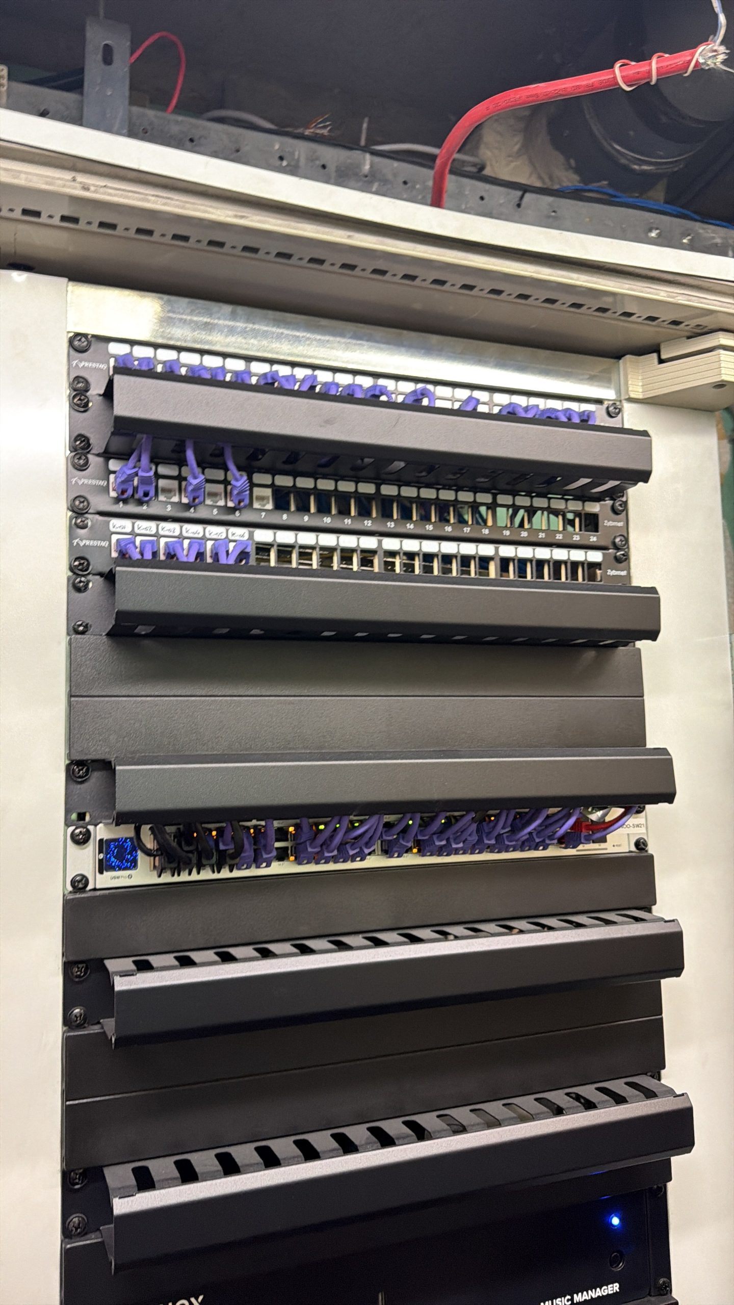 Netwerkkast in het pand met patchpanelen, een UniFi-switch met blauw display en nette paarse patchkabels