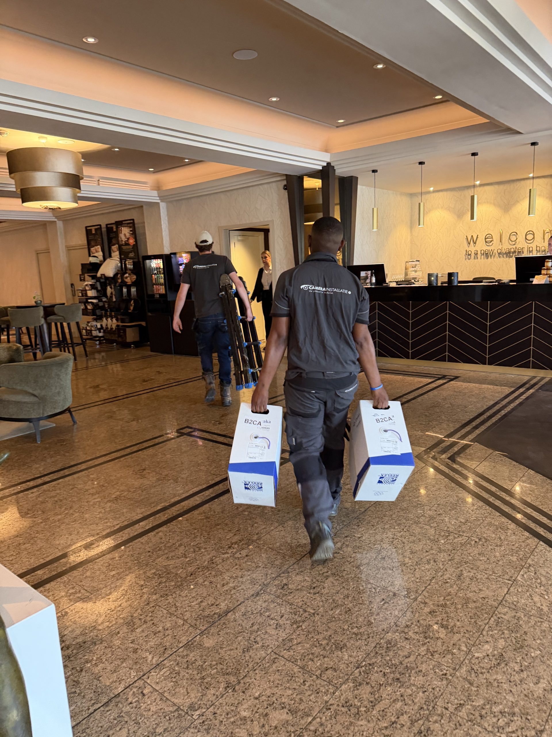 Twee monteurs van CameraInstallatie dragen dozen kabel door de lobby van een hospitality-locatie