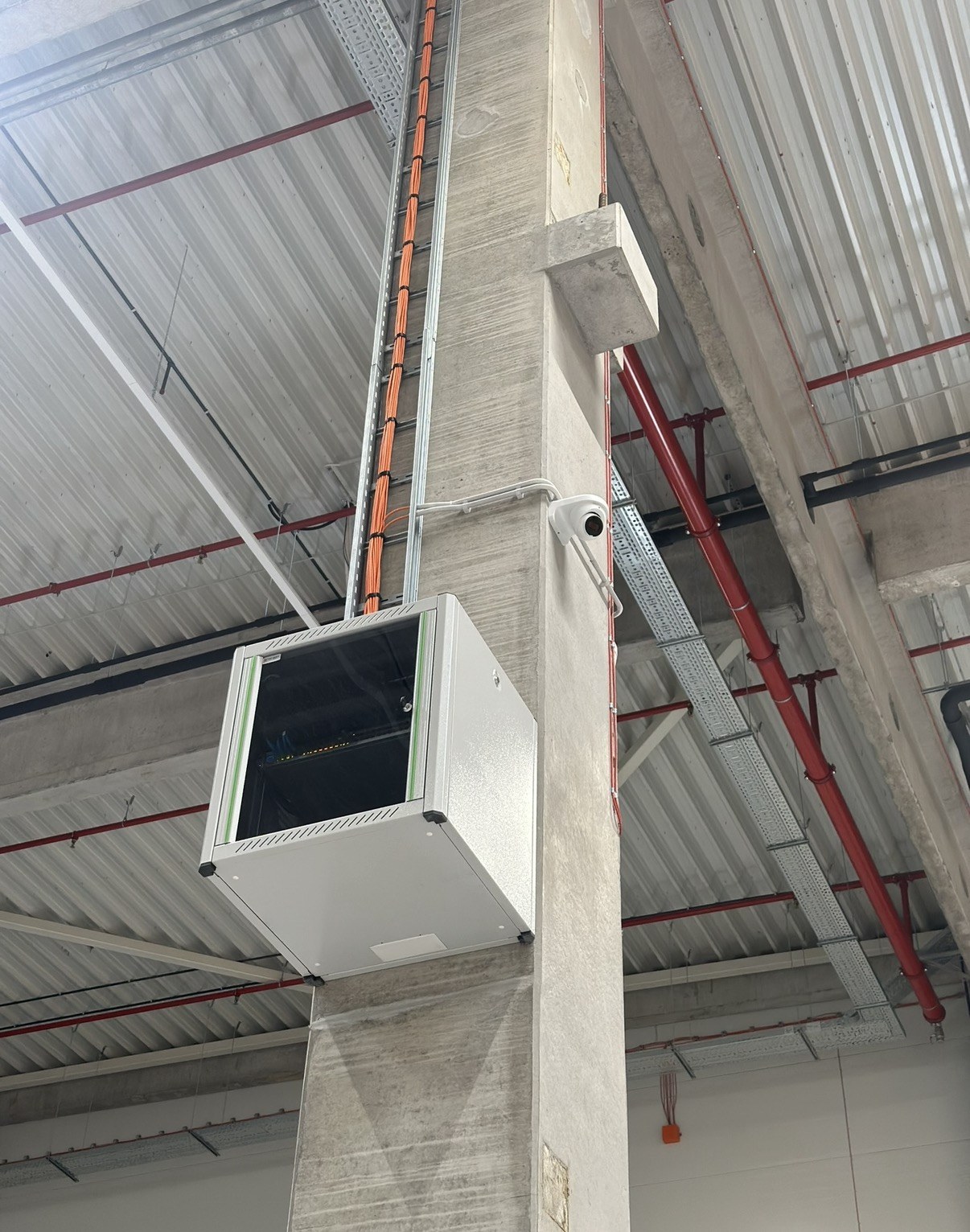 Wandpatchkast en dome-camera aan een betonnen kolom, met de oranje glasvezelbundel netjes in de kabelgoot omhoog