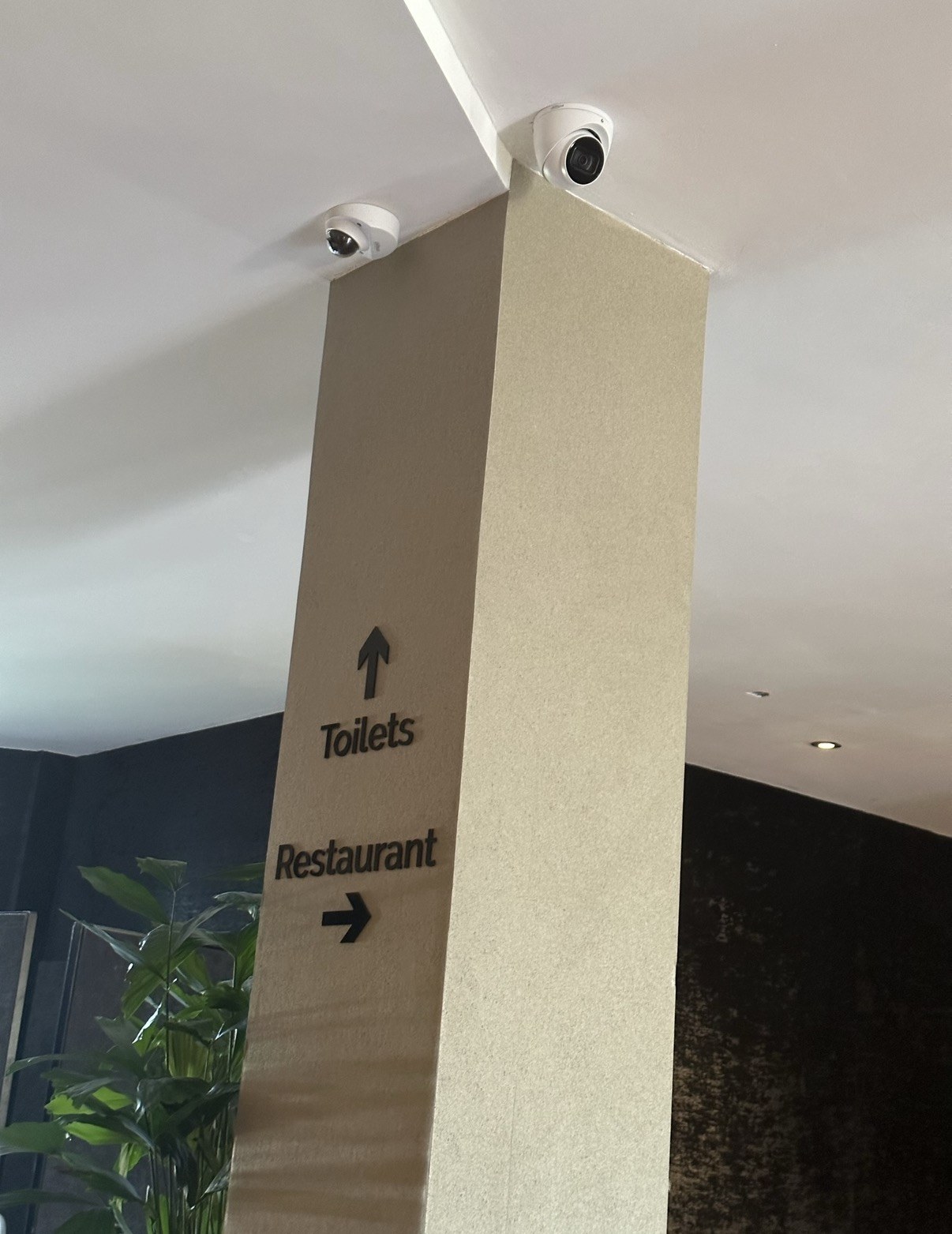 Twee camera's aan het plafond bij de zuil met bewegwijzering naar restaurant en toiletten
