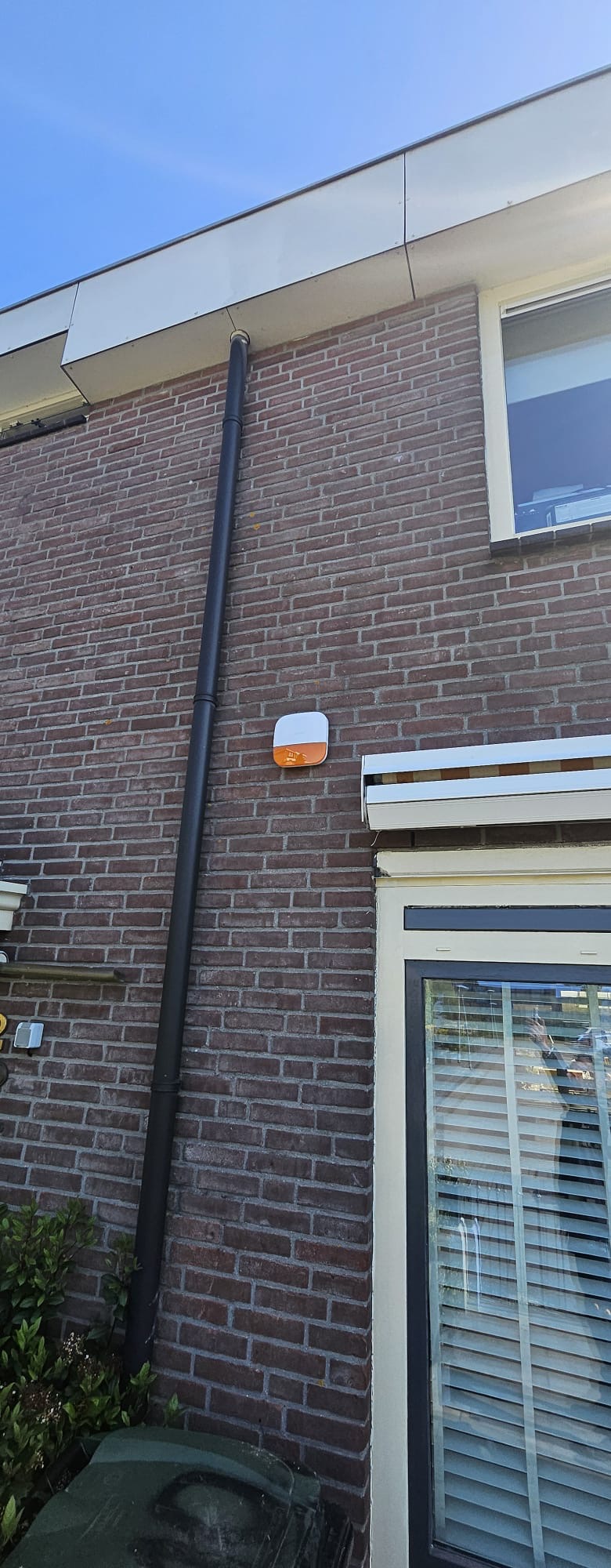 Draadloze buitensirene met flitslicht van het Dahua-alarm, gemonteerd hoog op de bakstenen gevel van het woonhuis