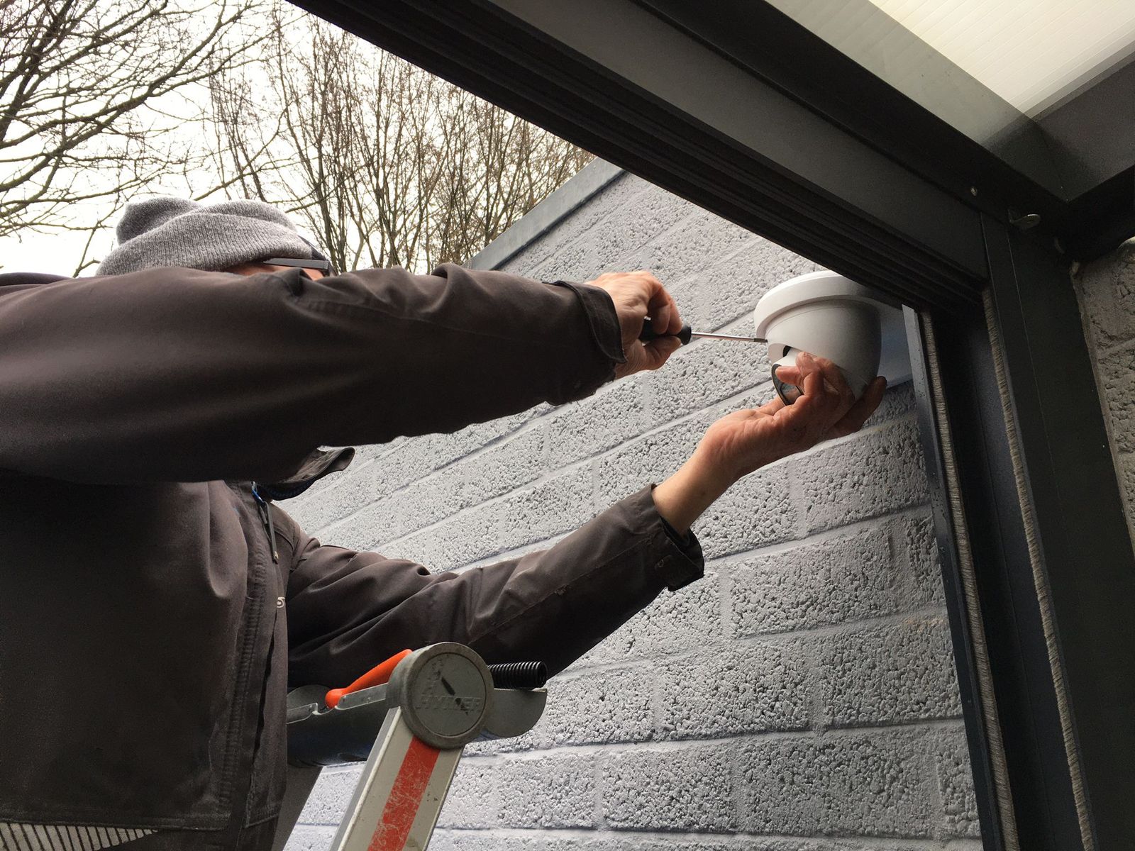 Monteur van CameraInstallatie monteert vanaf een ladder een camera aan een buitengevel