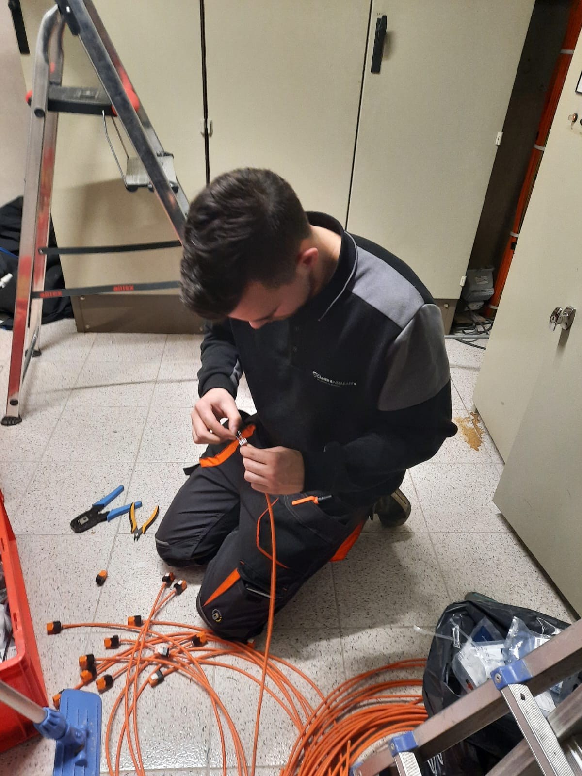 Monteur van CameraInstallatie monteert een connector op een oranje netwerkkabel in Hoofddorp