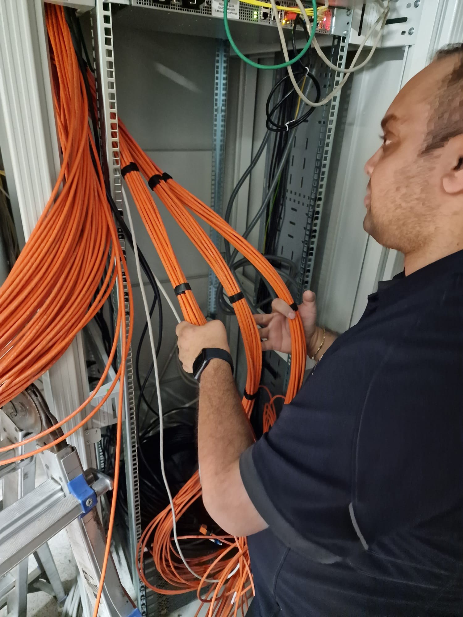 Monteur van CameraInstallatie bundelt oranje kwaliteitsnetwerkkabels netjes in een patchkast