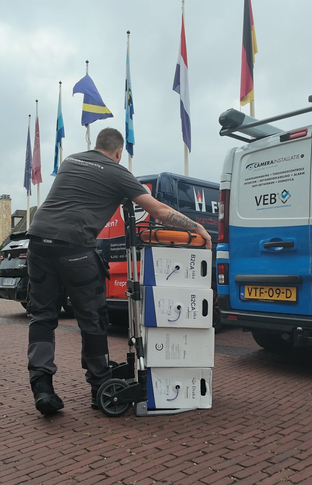 Monteur rijdt dozen netwerkkabel aan met een steekwagen, naast de bedrijfsbus met het VEB-keurmerk