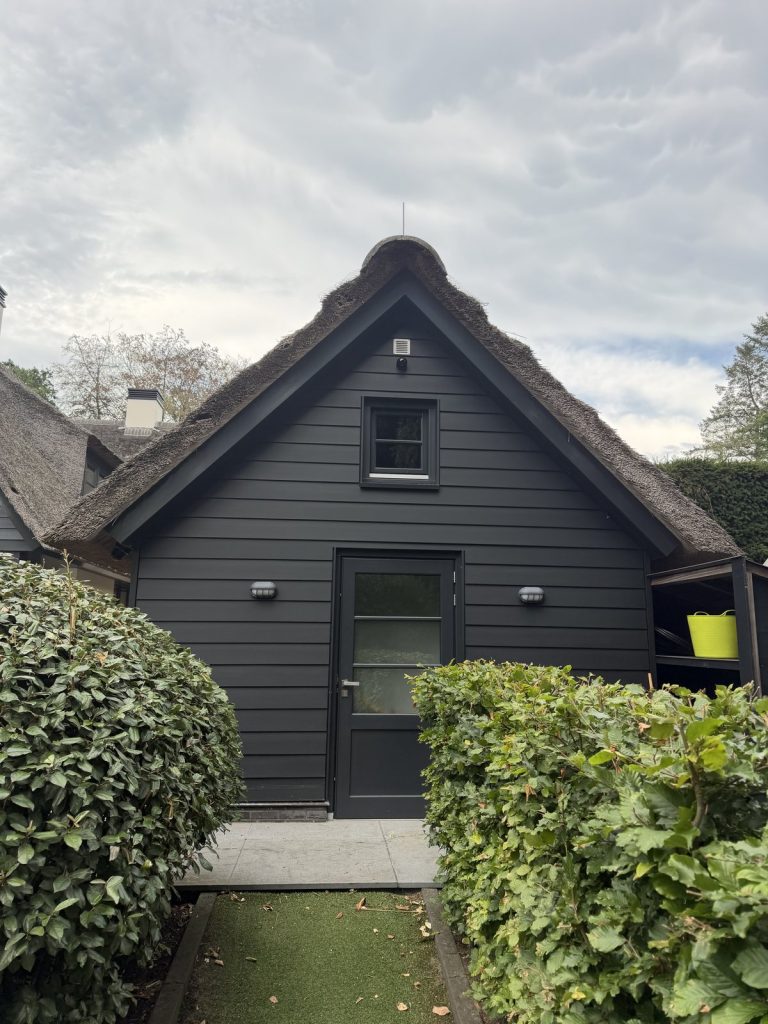 Rietgedekt bijgebouw waarop de camera vanaf afstand nauwelijks te zien is