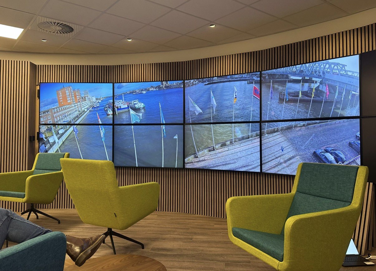 Grote videowall met live camerabeelden van een haven, opgehangen in een ruimte met loungestoelen