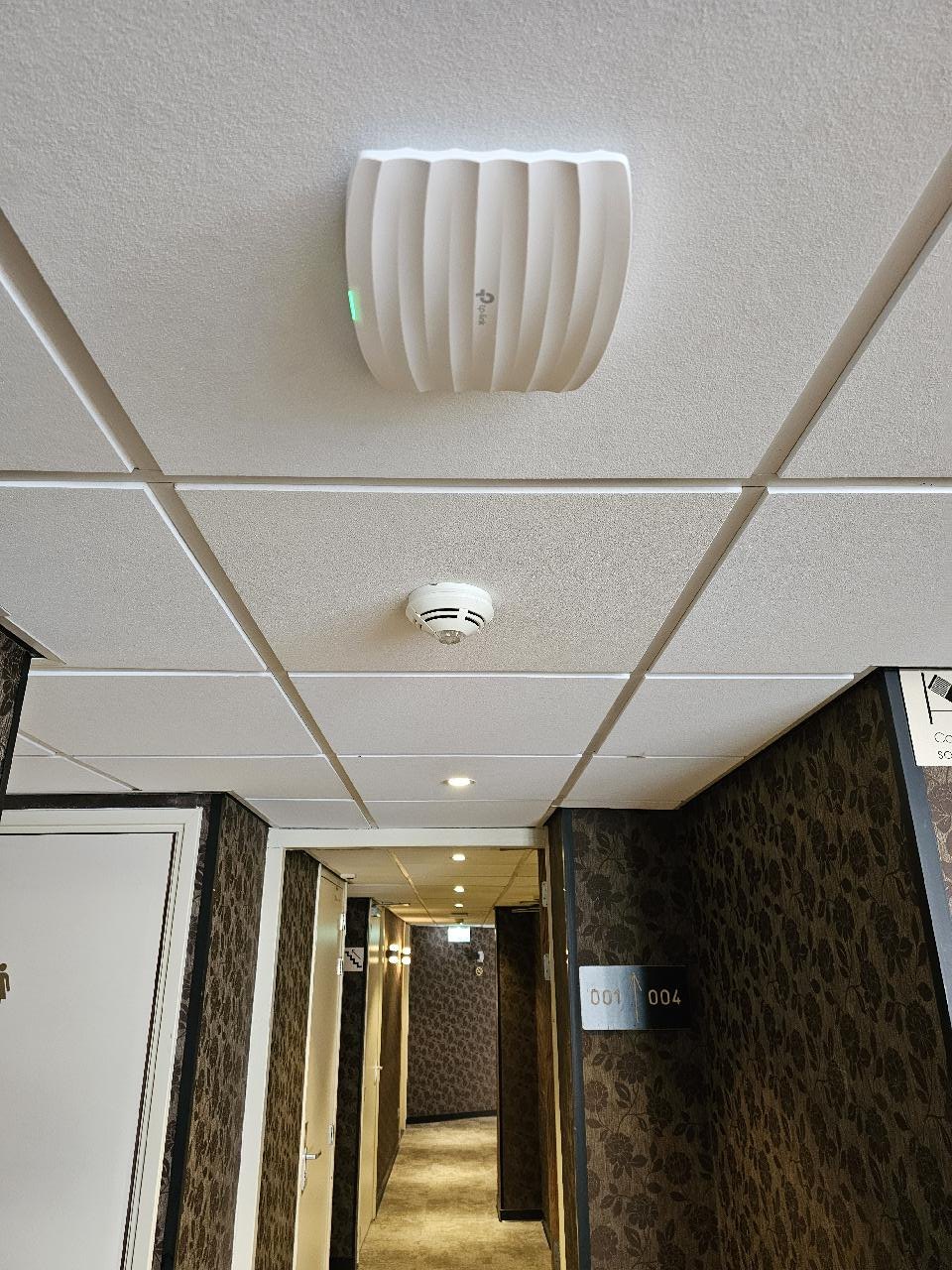 Wit access point aan het plafond van een hotelgang met donker behang