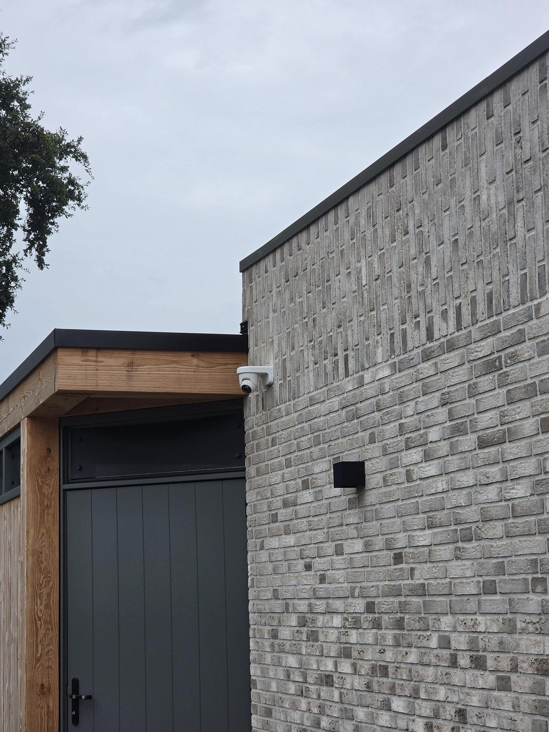 Witte Ajax-camera op een muurbeugel onder de dakrand bij de carport van de woning