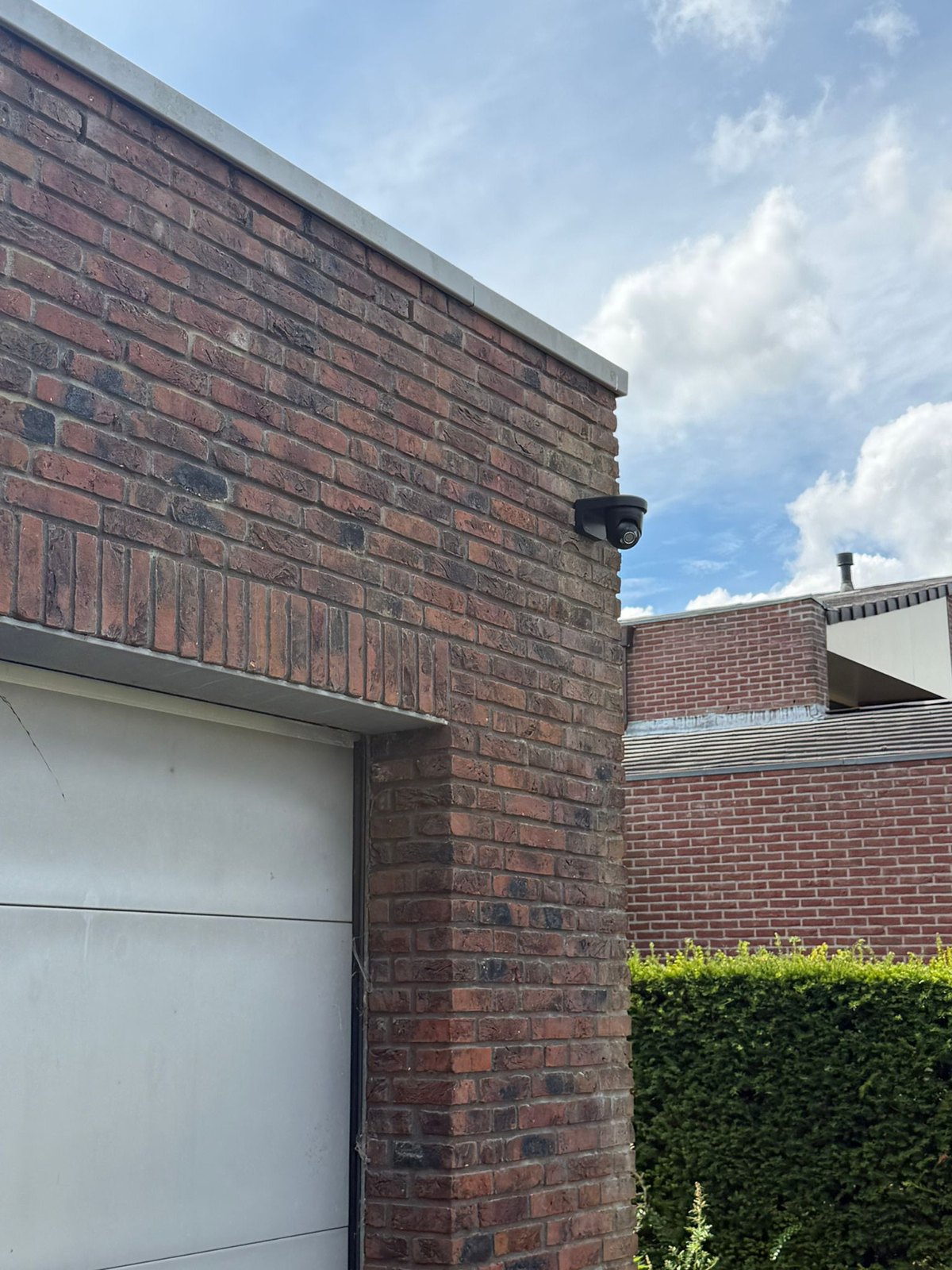 Zwarte beveiligingscamera op de bakstenen hoekkolom boven de garagedeur van een vrijstaande woning