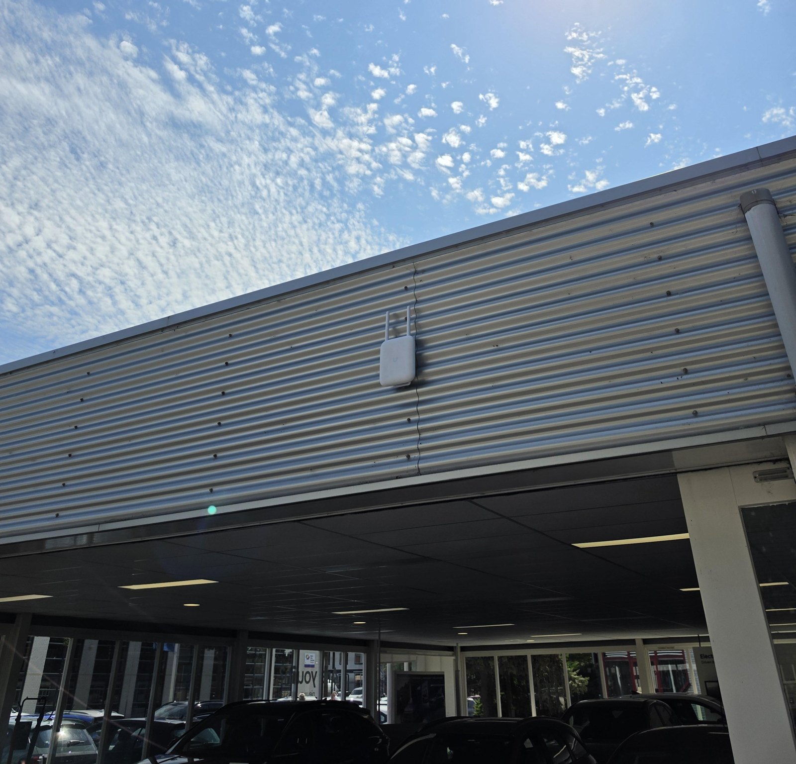 Wit buiten-access point op de metalen gevel boven een overkapping met geparkeerde auto's