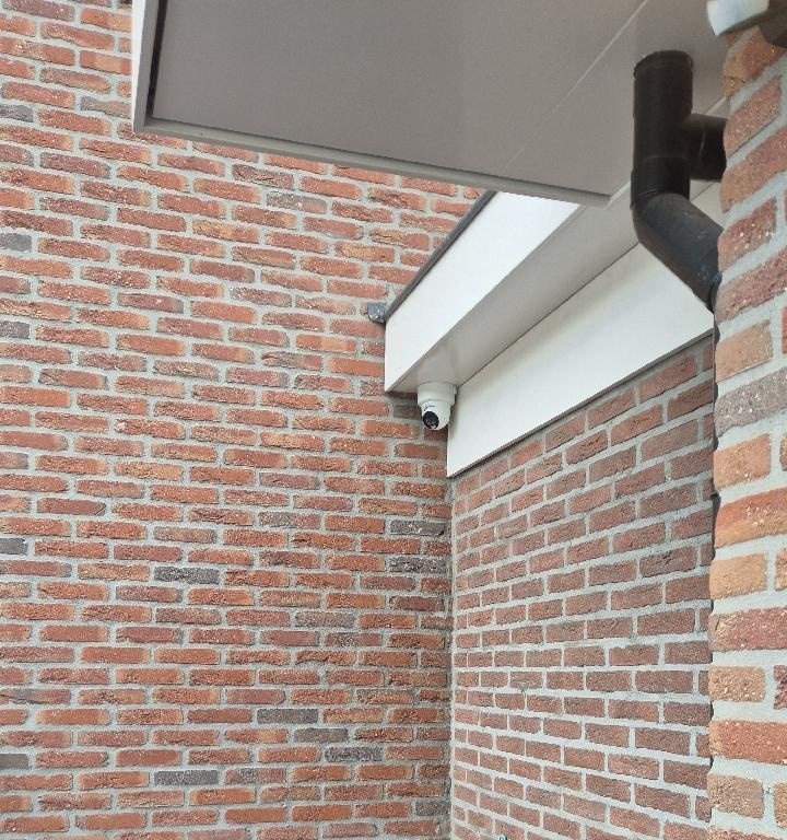 Witte turretcamera onder de dakrand in de hoek tussen twee bakstenen gevels