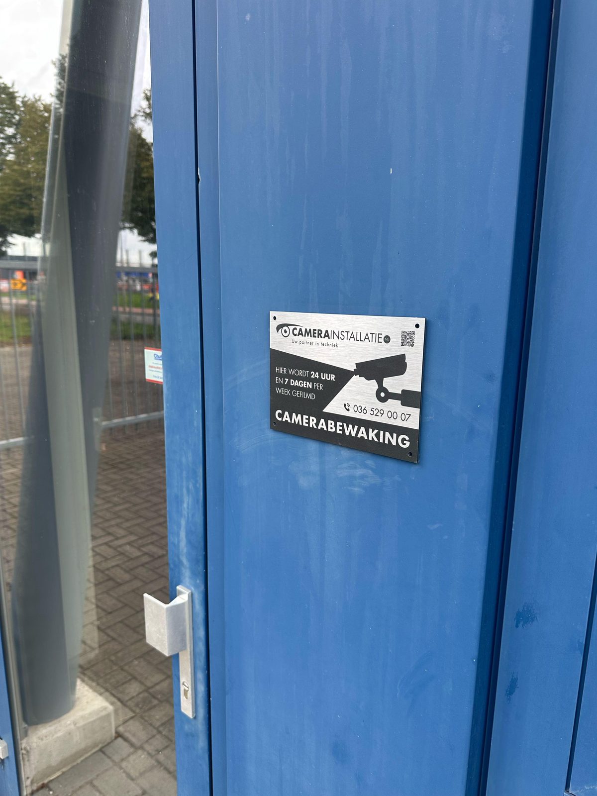 Parkeerbord eigen terrein met daaronder een bord camerabewaking van CameraInstallatie.nl, met de loods op de achtergrond