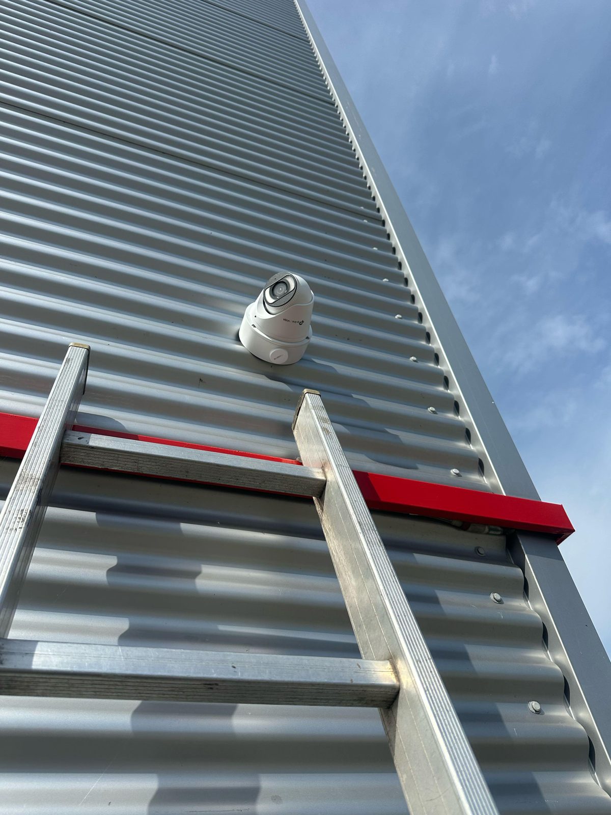 Witte VIGI-camera hoog op de golfplaten gevel van een loods in Roosendaal, met de ladder er nog tegenaan