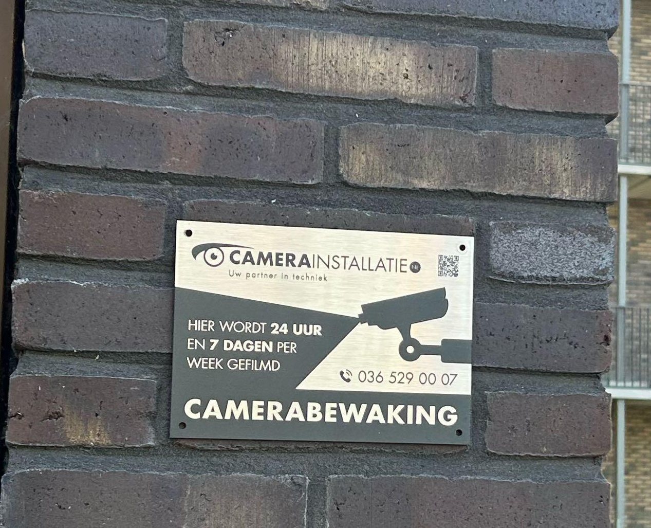 Metalen bord camerabewaking van CameraInstallatie.nl op een bakstenen pilaar bij de ingang