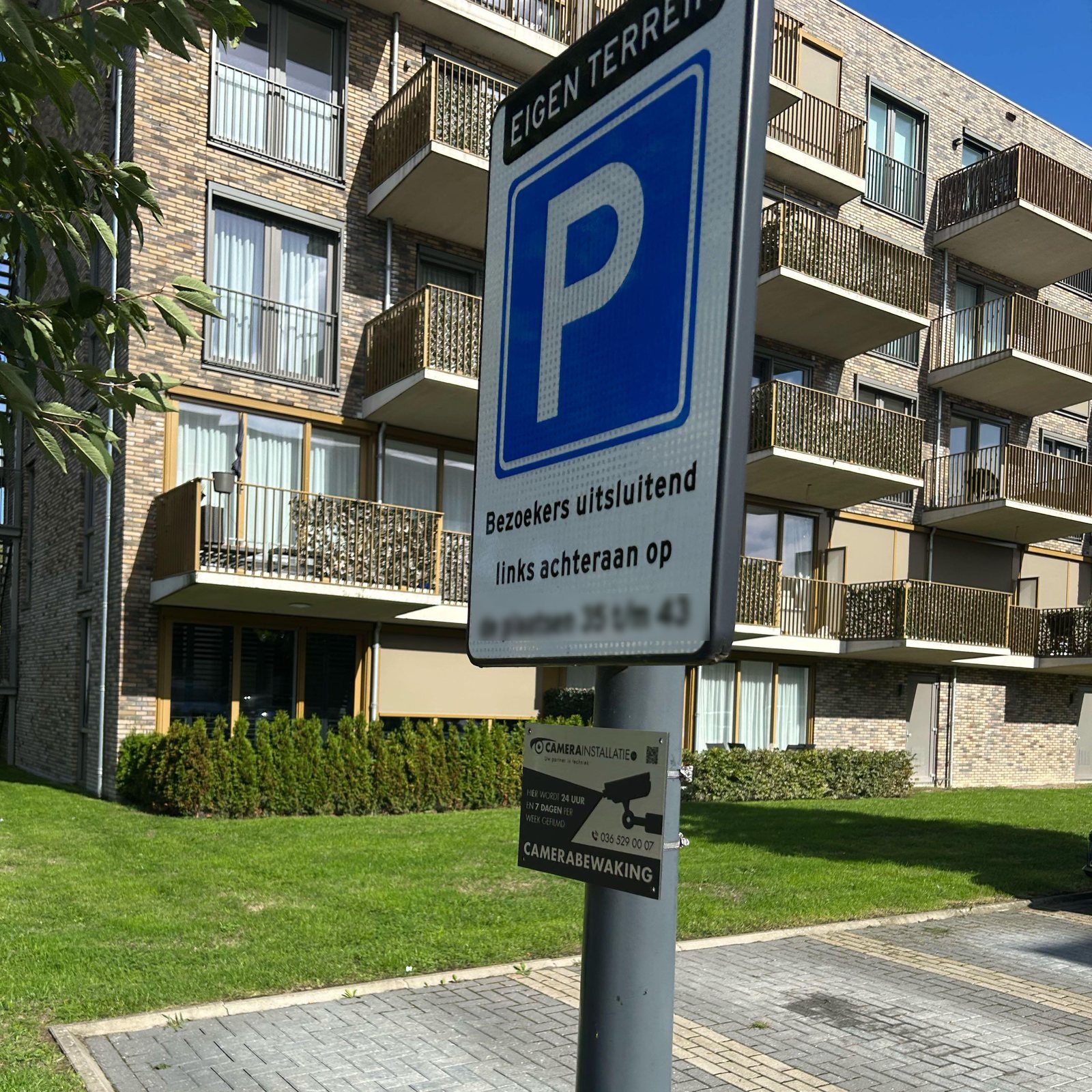 Parkeerbord eigen terrein met daaronder een bord camerabewaking van CameraInstallatie.nl, met het appartementencomplex op de achtergrond