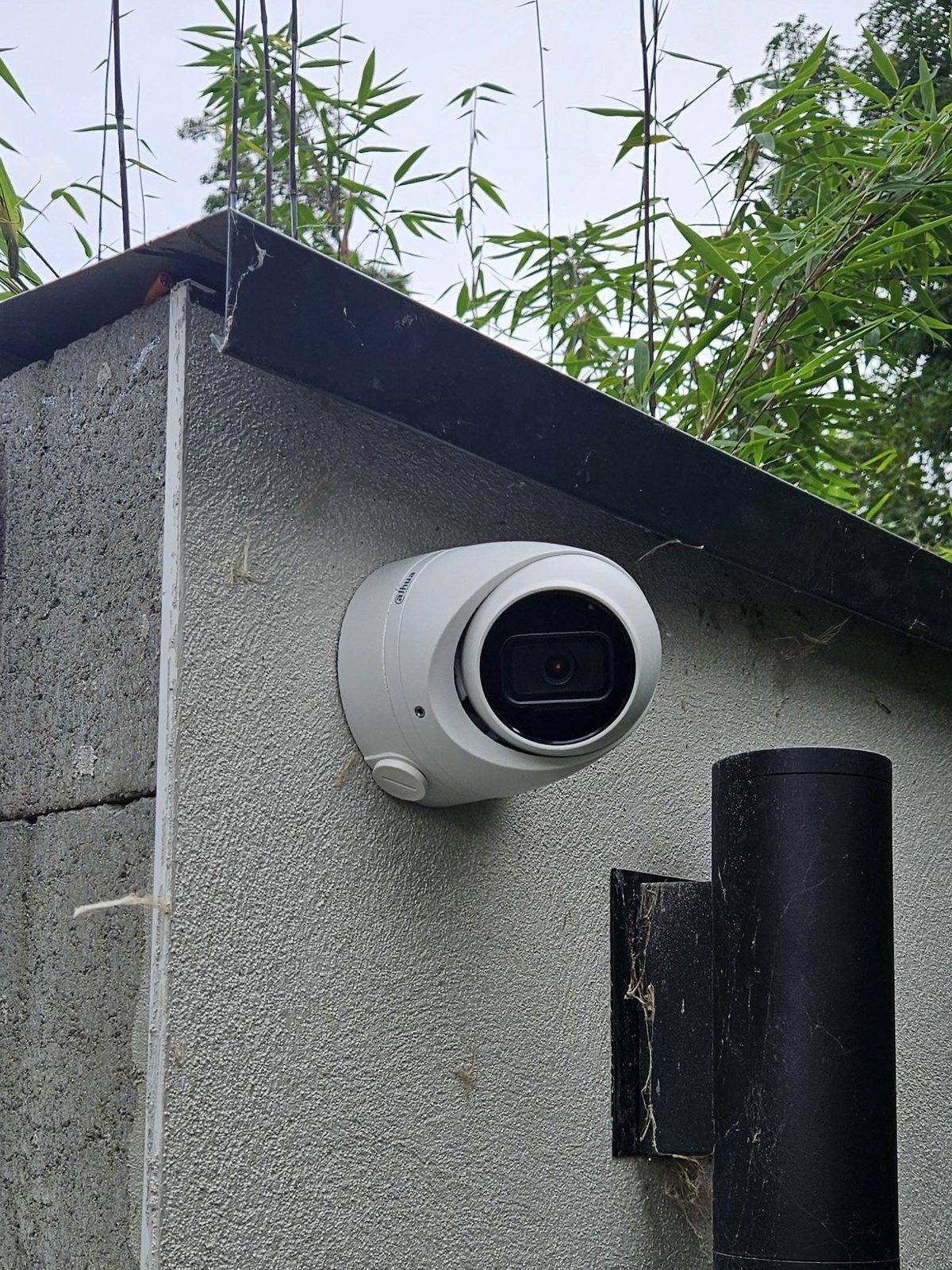 Dichtbij: de witte Dahua-camera onder de muurafdekking bij de achterpoort