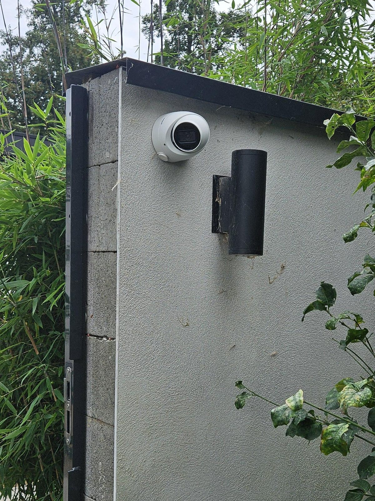 Witte Dahua-camera op de muur naast de poort, gericht op de steeg achter de tuin