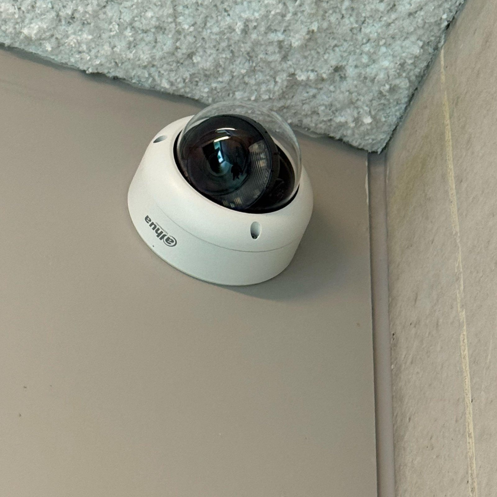 Witte Dahua-domecamera in de hoek van een ruimte, vlak onder het plafond