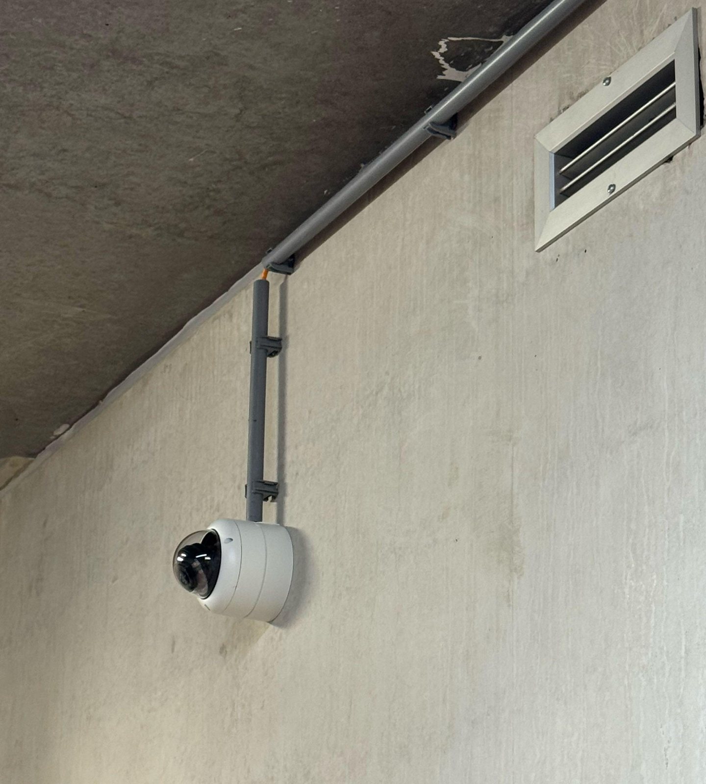 Witte Dahua-domecamera hoog op een betonwand, de kabel loopt in een grijze pvc-buis vanaf het plafond