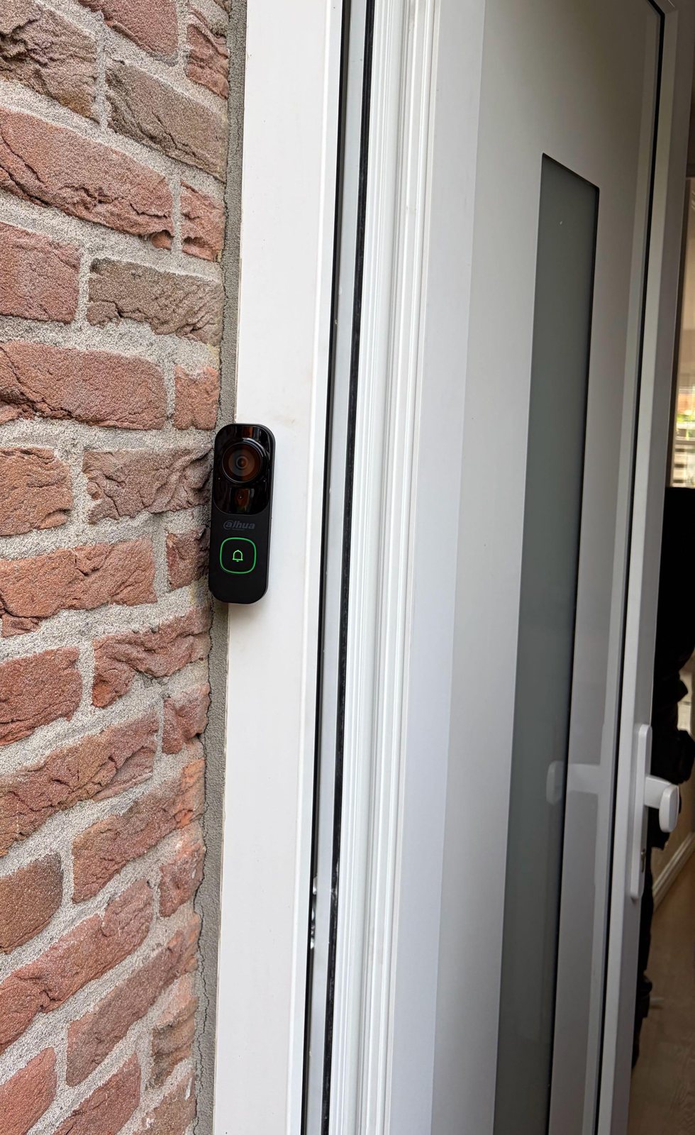 Zwarte Dahua-videodeurbel met groen verlichte belknop op het kozijn naast de voordeur