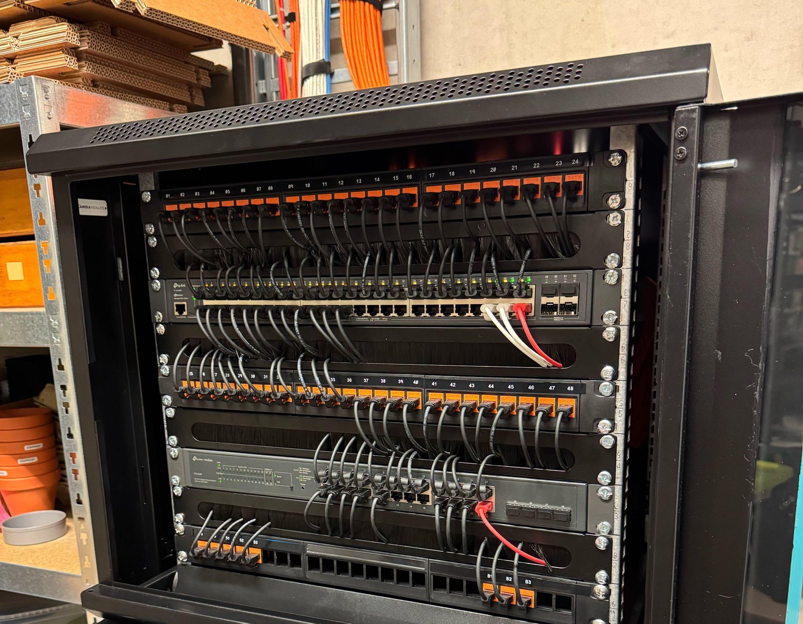 Open 9U-patchkast met twee switches en patchpanelen met oranje keystones, de kabels strak in bundels gelegd