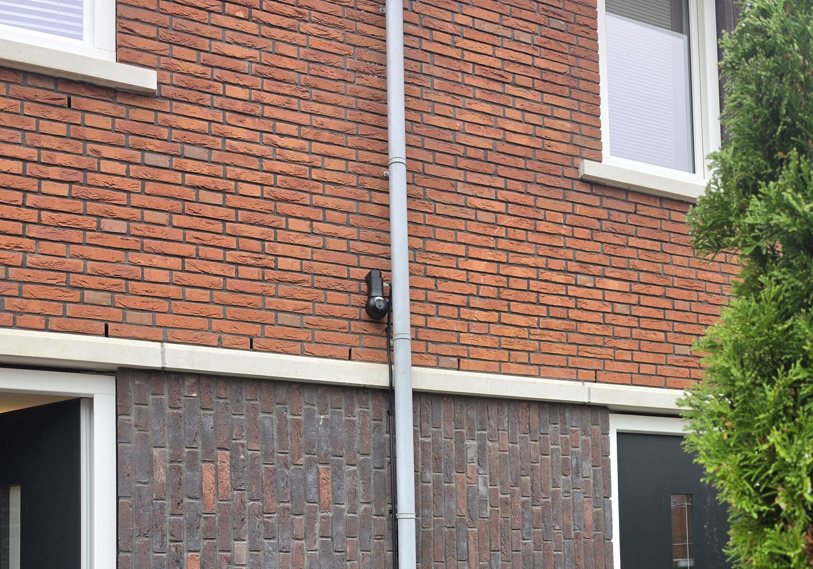 Achtergevel van een woning in Ridderkerk met de zwarte UniFi-camera tussen de verdiepingen, naast de regenpijp