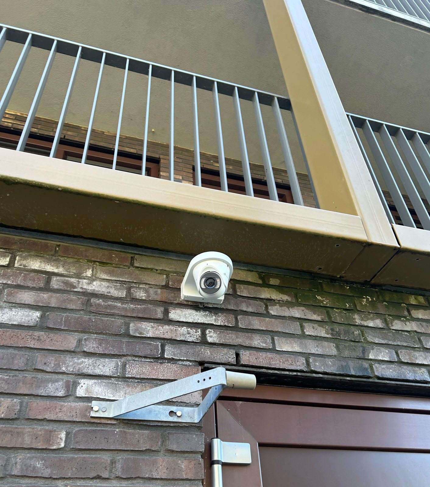 Witte VIGI-camera van 8 megapixel met full color onder de galerij van een appartementencomplex, boven een deur