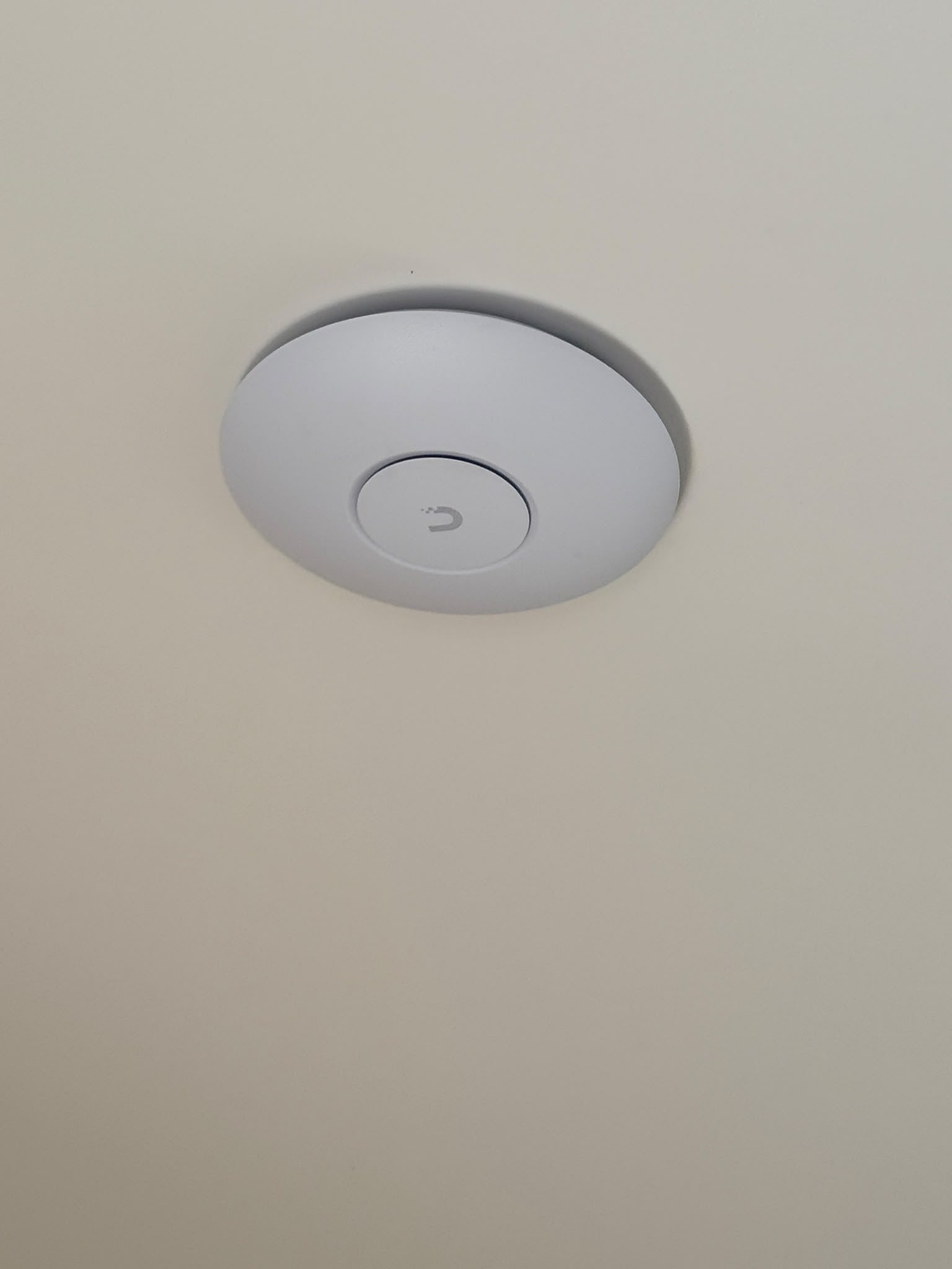 Wit UniFi access point strak tegen het plafond gemonteerd