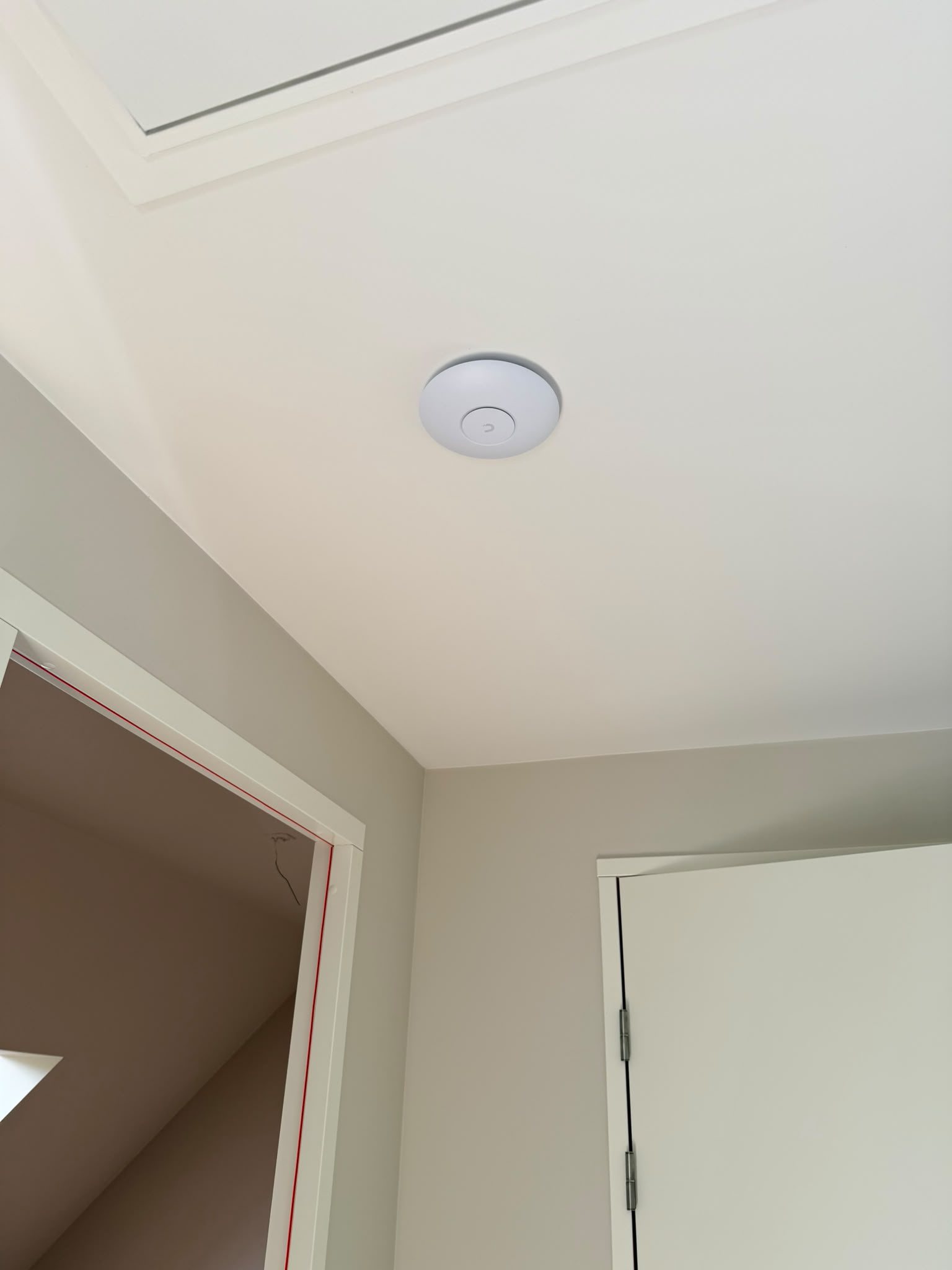 UniFi access point aan het plafond van de overloop op de tweede verdieping, naast het zolderluik